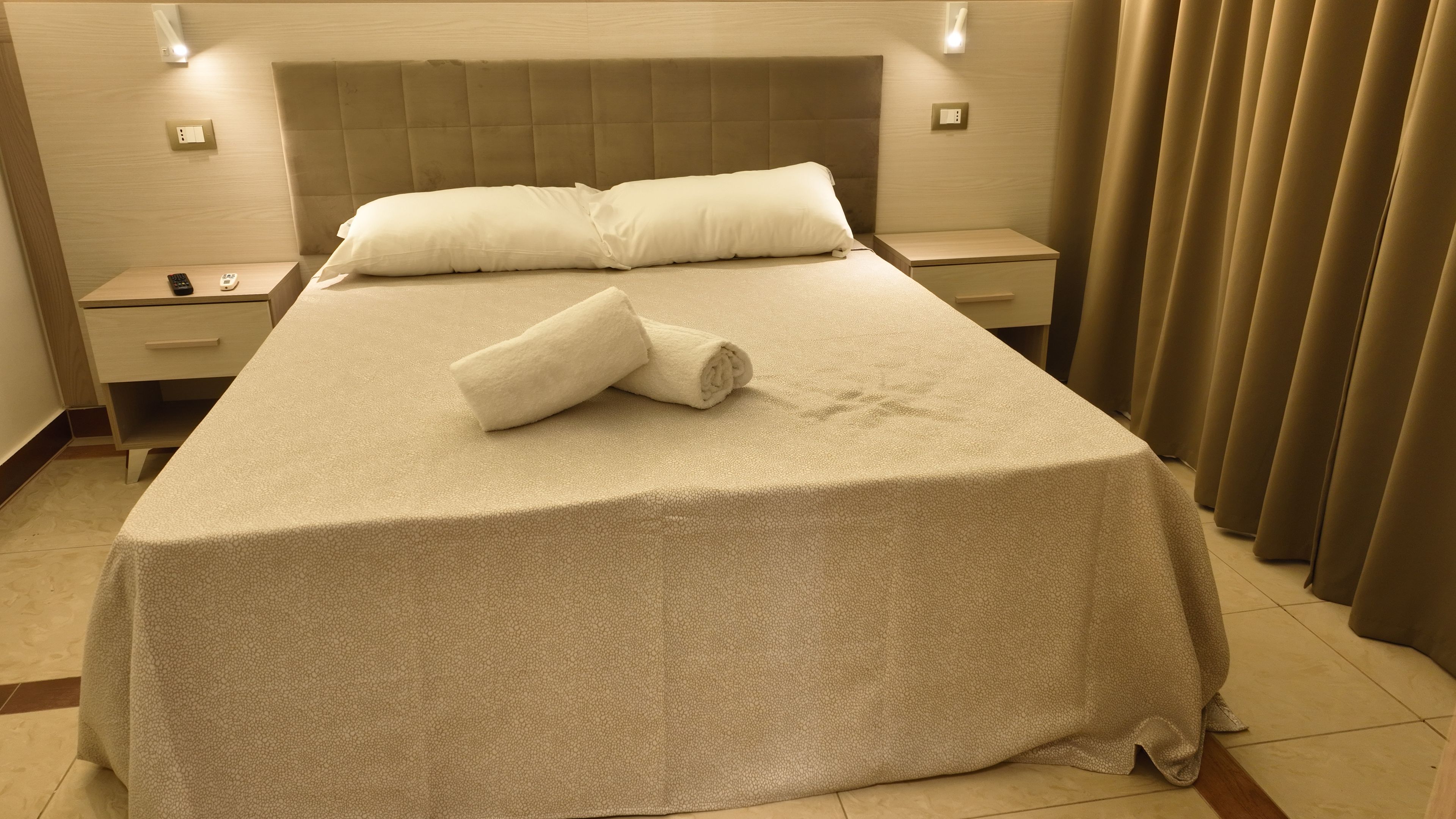 Una habitación de hotel con cama, mesita de noche, lámpara y cortina.