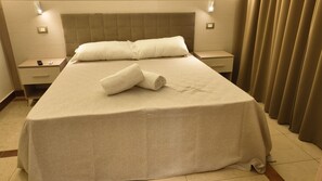 Una habitación de hotel con cama, mesita de noche, lámpara y cortina.