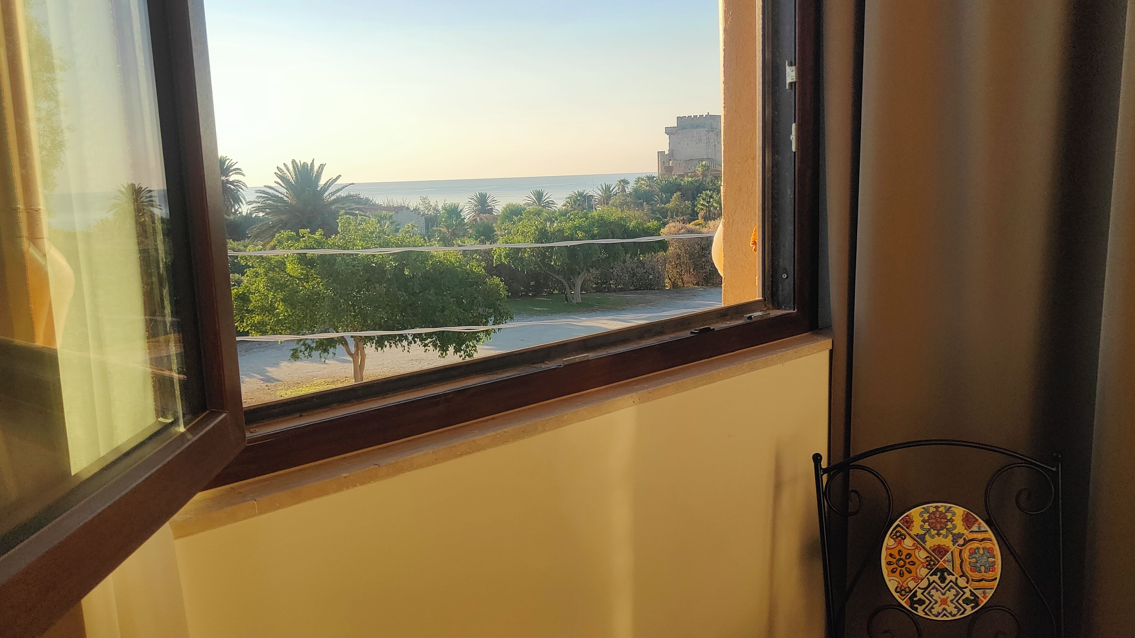 Ein Fenster mit Blick auf eine Küstenlandschaft, darunter Bäume und ein entferntes Gebäude.