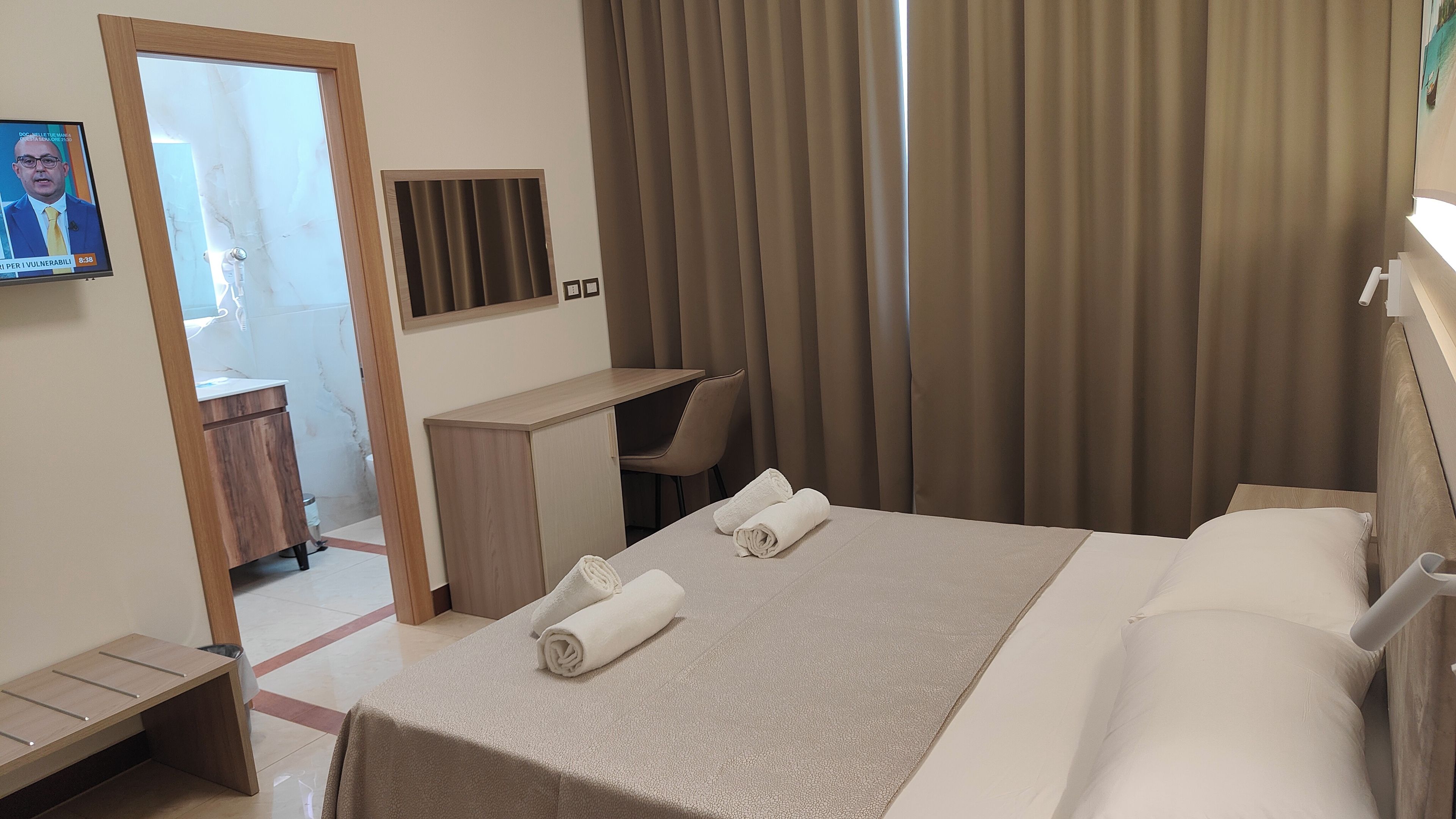 A hotel room with a bed, a desk, a chair, and a television.