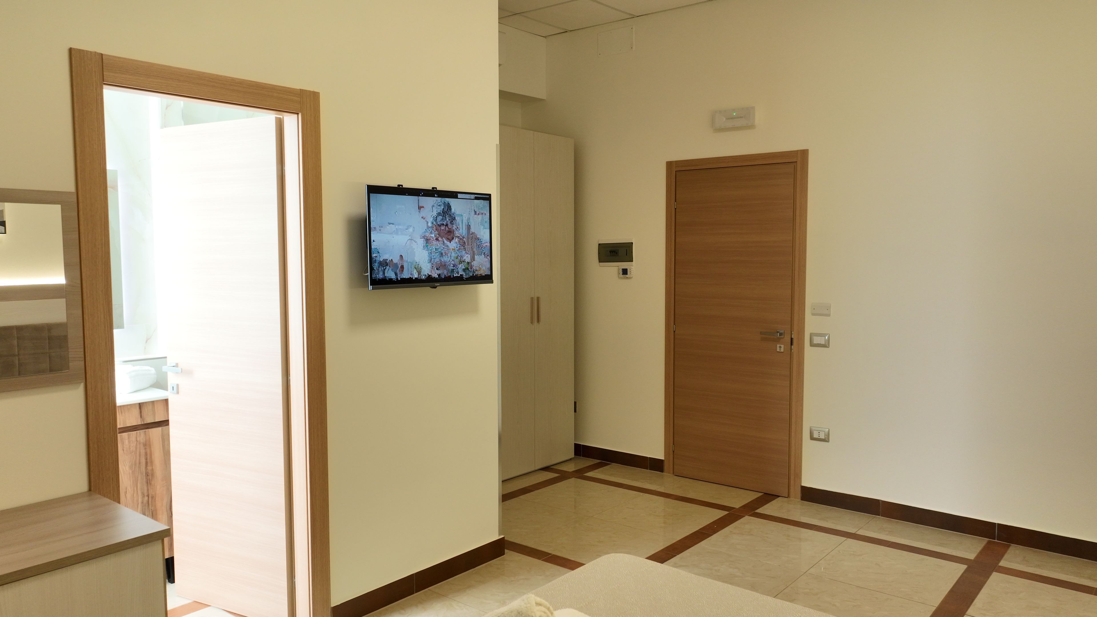 Un pasillo de hotel con un televisor montado en la pared, una puerta de madera y suelo de baldosas.
