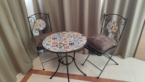 A small round table with a colorful tile pattern, two chairs with woven seat cushions, and a metal frame.