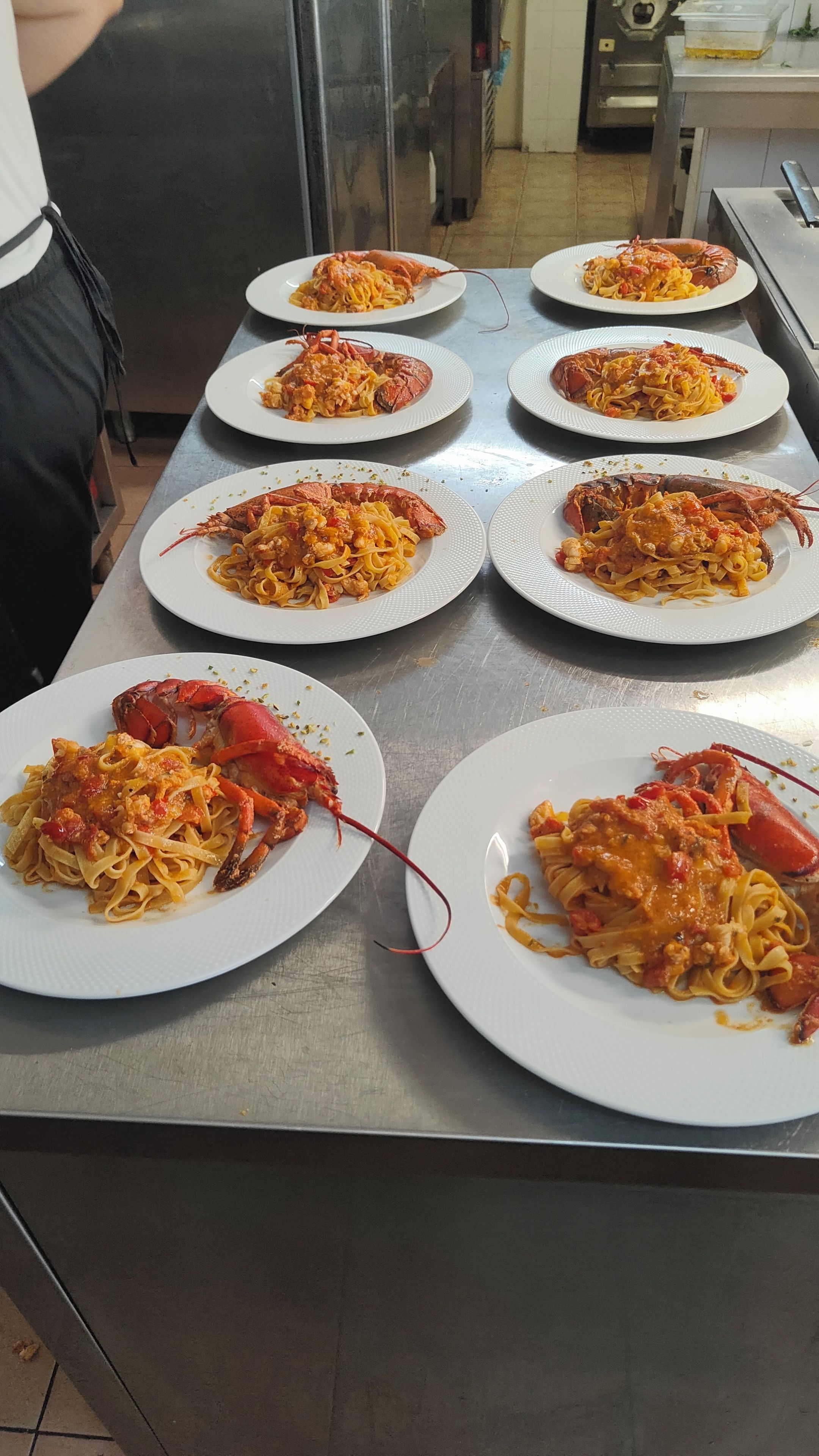 Une table en acier inoxydable sur laquelle sont disposés plusieurs assiettes de pâtes et de homard.