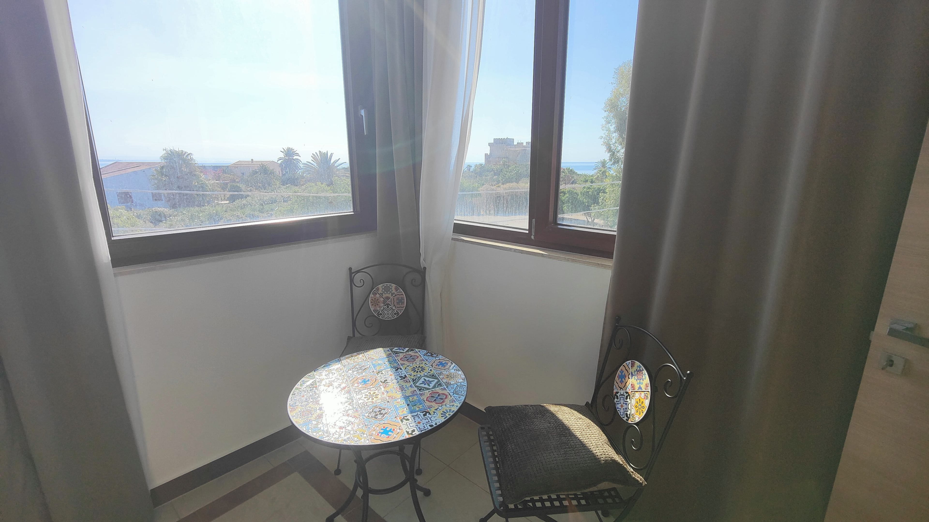 Une pièce d’angle avec une petite table et une chaise, une vue sur l’extérieur et une fenêtre avec des rideaux.