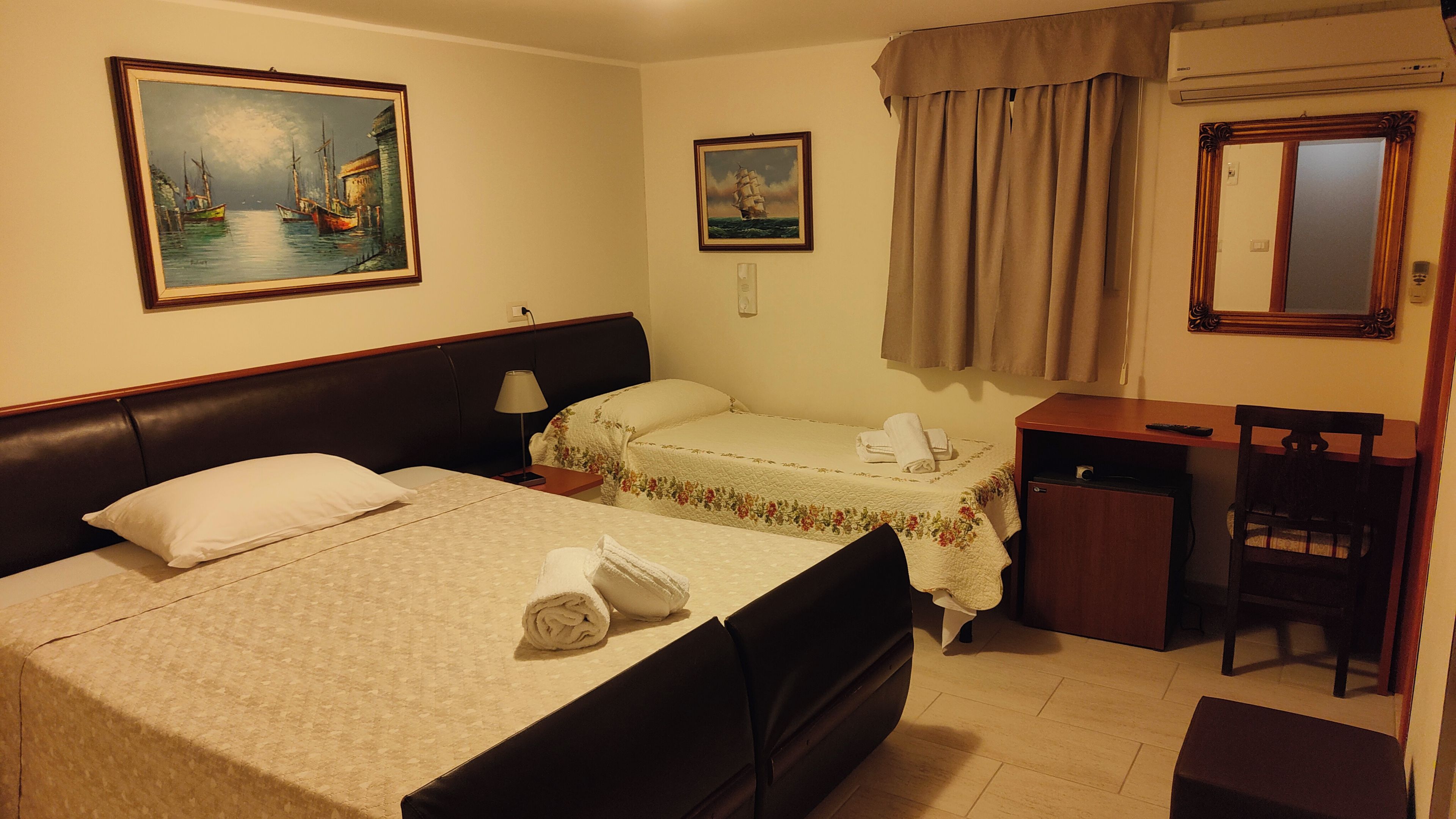 Habitació d'hotel amb llit, escriptori, cadira, mirall i dos quadres penjats a la paret.