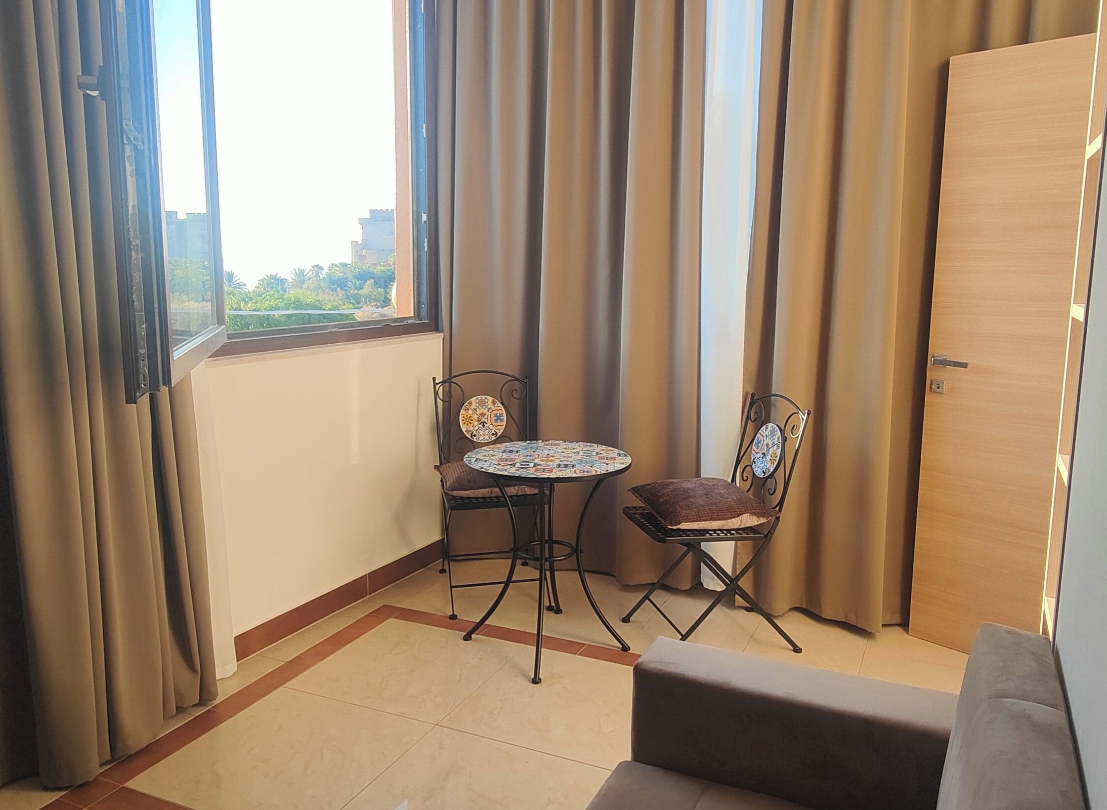 A small room with a window, a table, two chairs, a door, and a sofa.