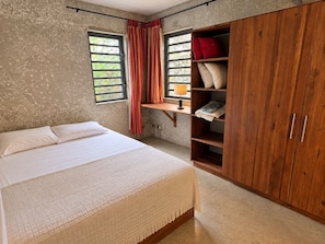 A bedroom with a bed, a wooden wardrobe, a shelf with pillows, and a window with curtains. - Villa Colibris – Your Peaceful Haven with Pool (Grand Baie)