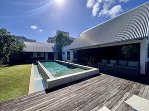 Ein moderner Poolbereich im Freien mit einer Holzterrasse, einem rechteckigen Pool und einer überdachten Lounge-Ecke.