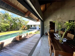 A modern indoor space with a pool, wooden deck, and a dining area with a view of the outdoors. - Villa Colibris – Your Peaceful Haven with Pool (Grand Baie)