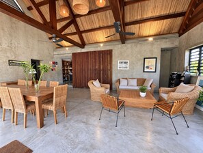A spacious room with a high ceiling, a dining area with a wooden table and chairs, a sofa set, and a large window providing natural light. - Villa Colibris – Your Peaceful Haven with Pool (Grand Baie)