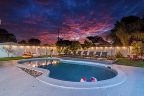 Piscina com espreguiçadeiras e céu ao pôr do sol.