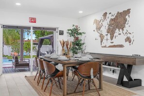 A dining area with a wooden table set for four, surrounded by chairs, a world map on the wall, and an exit sign. - Heated Pool + Backyard Fun + Sleeps 12 + 15 Min to the Beach (Hollywood)