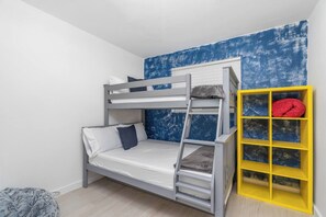 Ein Stockbett mit einer Stehle, ein kleines Regal mit einem roten Gegenstand und ein gemustertes Teppich.