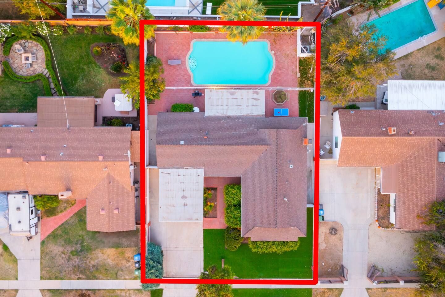 An aerial view of a residential area with a swimming pool, a patio, and a well-maintained lawn.