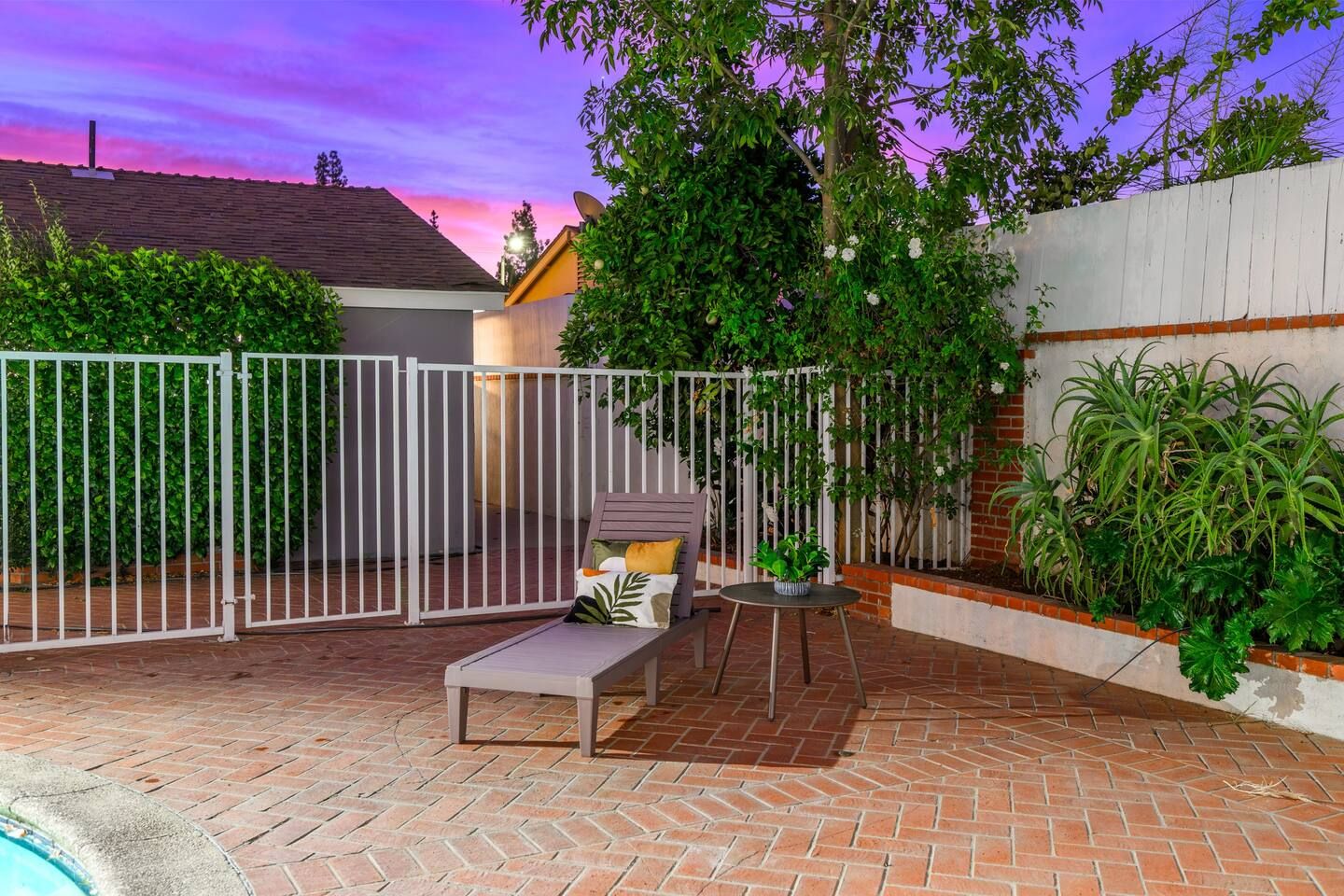 Un patio con piscina, un recinto bianco e una sedia a sdraio.