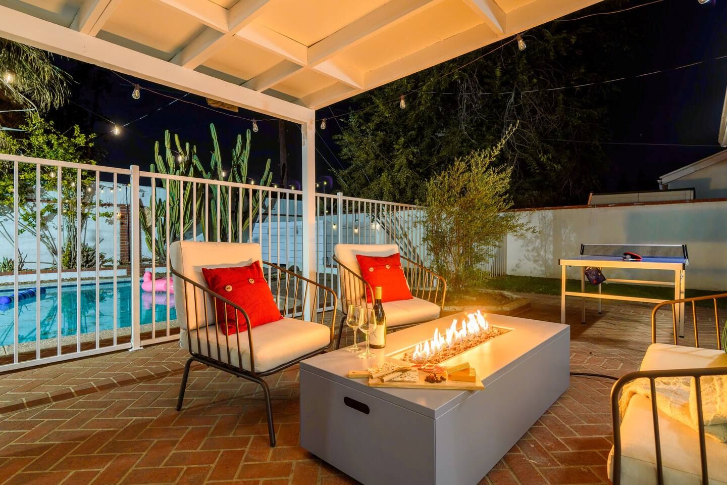Eine Außenpatio mit Pool, zwei Stühle mit roten Kissen, ein Tisch mit Flasche und Gläsern sowie ein Tischtennisplatte.