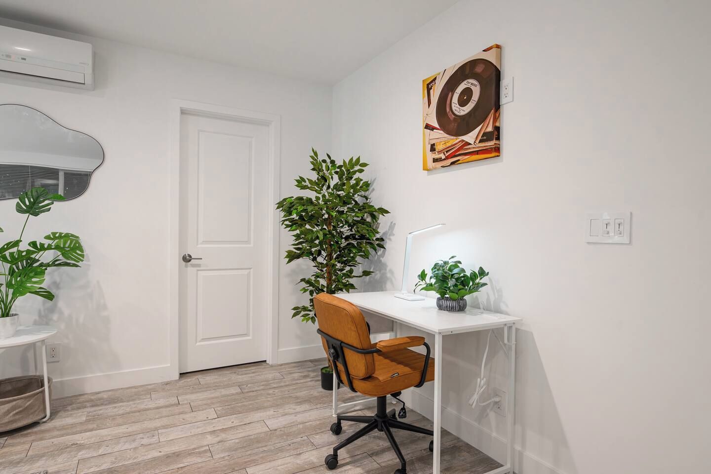 Ein moderner Arbeitsraum mit Schreibtisch, Stuhl, Topfpflanzen und einem Wandbild.