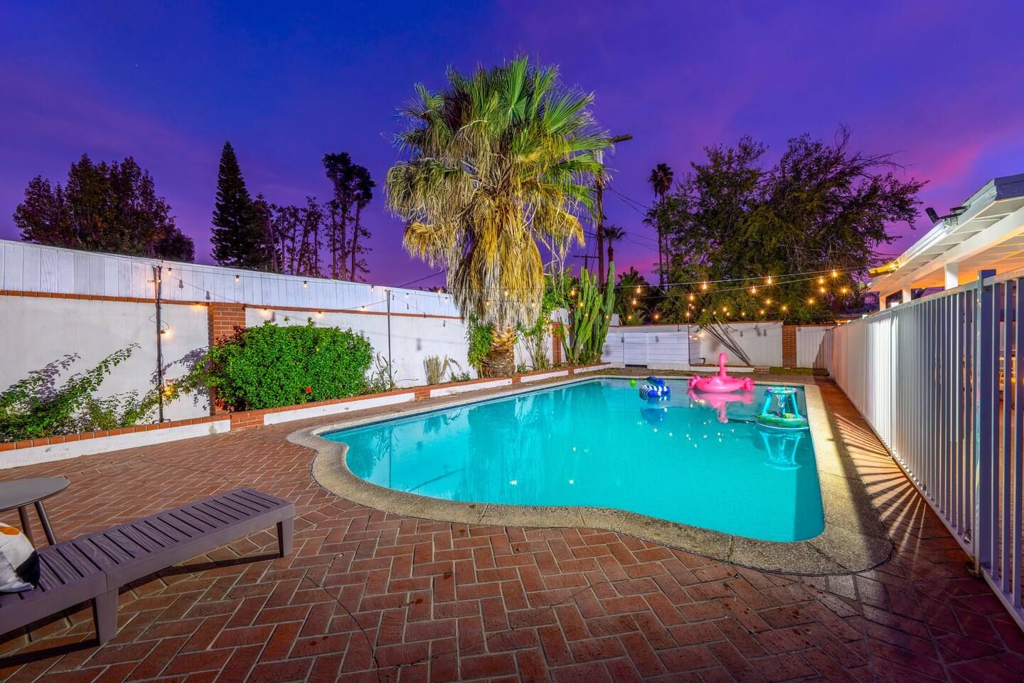 Ein Schwimmbecken mit Pflasterterrasse, Liegestühlen und Lichterketten.
