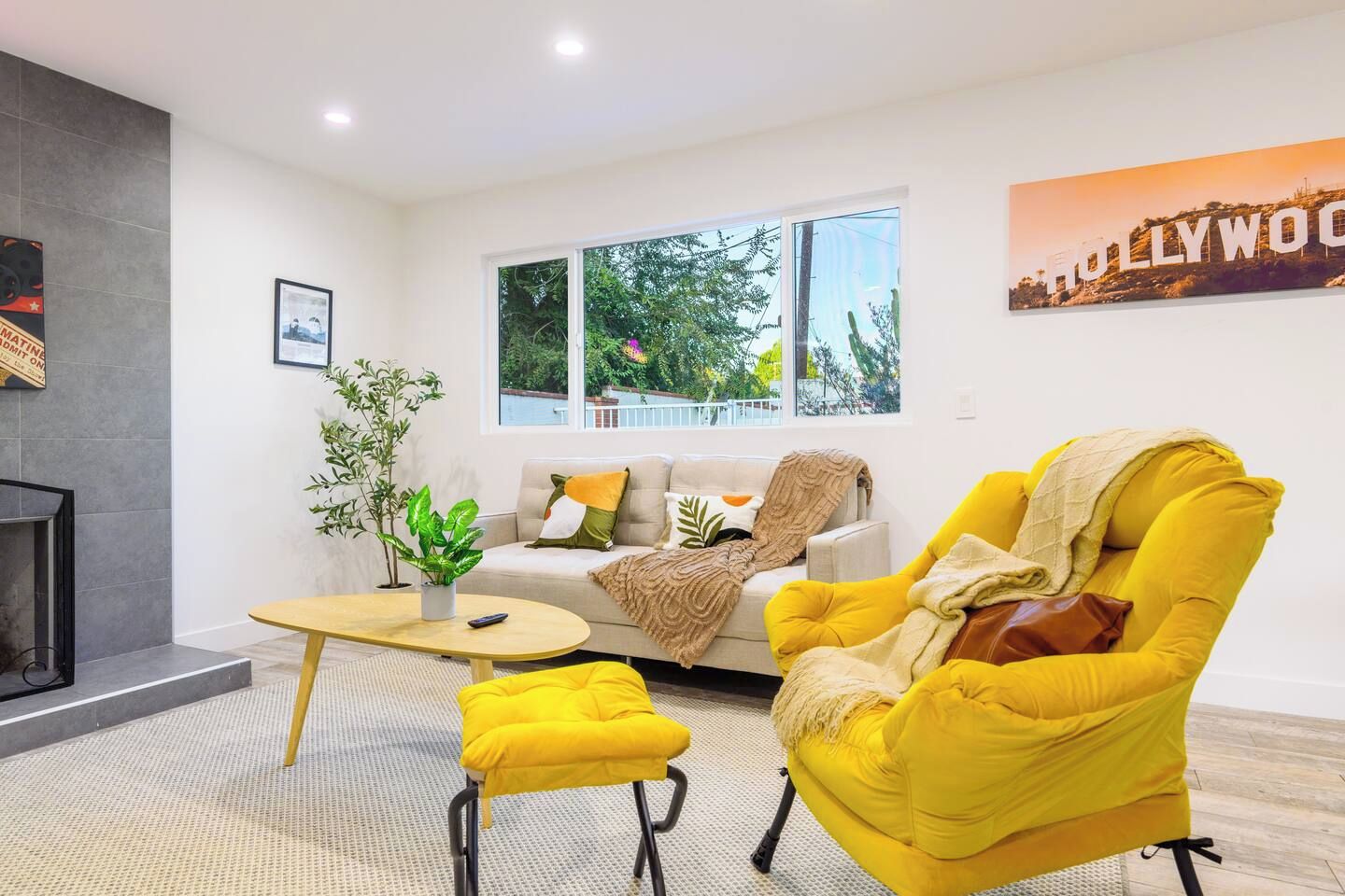 Een woonkamer met een bank, een gele fauteuil, een salontafel en een open haard.