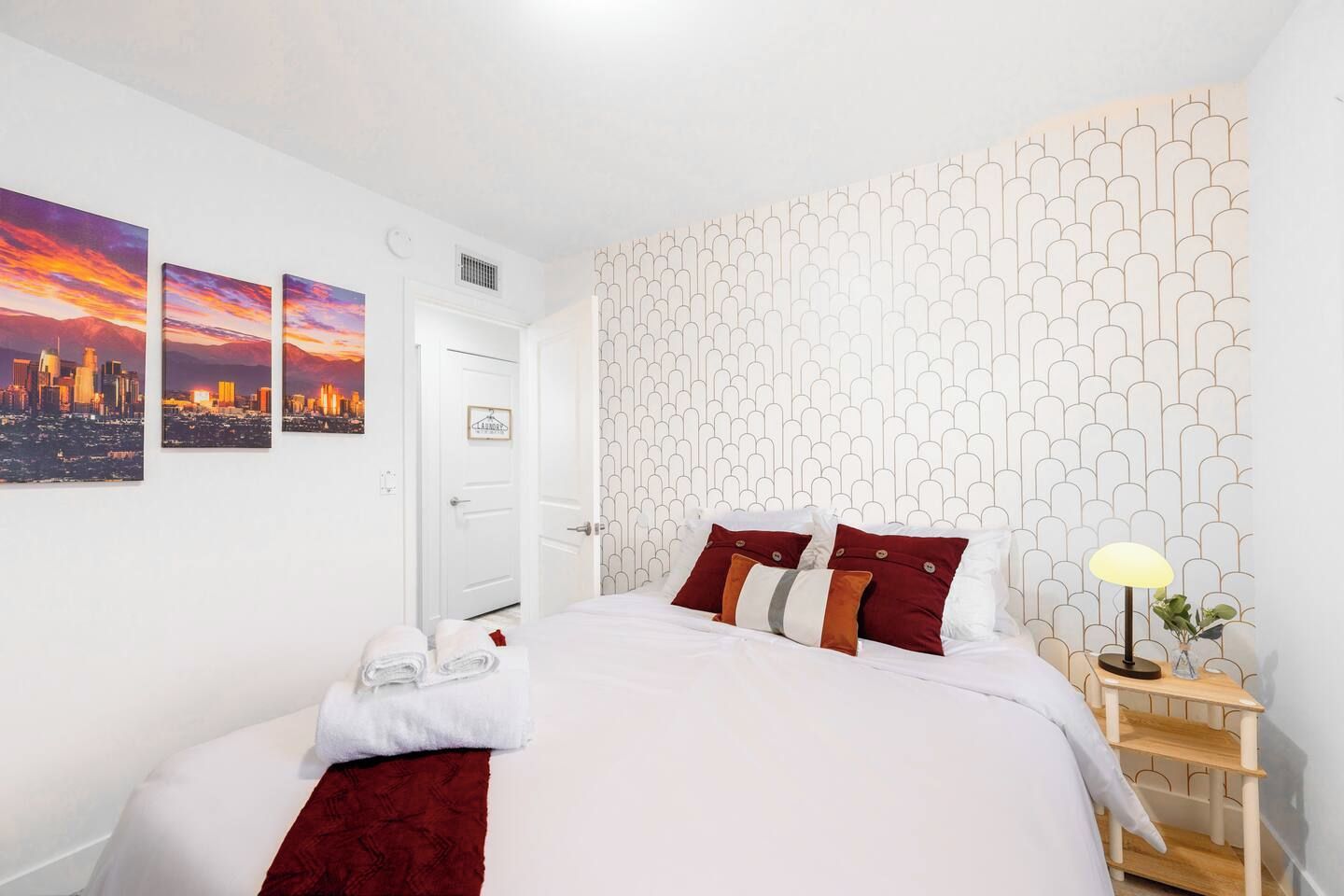 Ein Hotelzimmer mit einem Bett, einem Nachttisch, einer Lampe und drei Stadtansichten an der Wand.