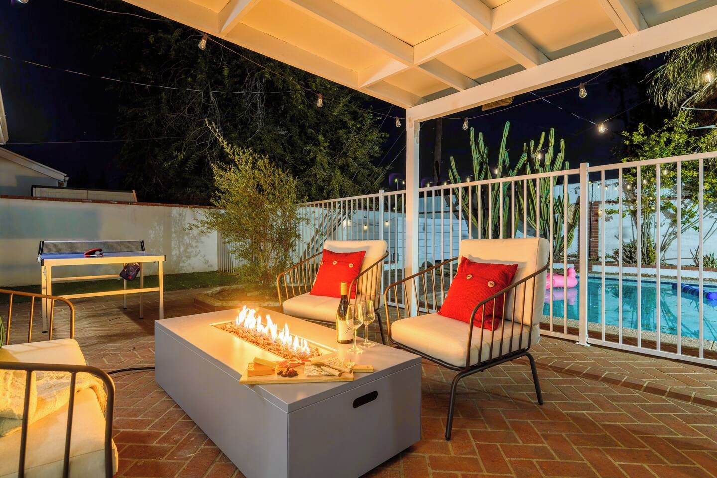 En udendørs terrasse med bålsted, siddepladser og swimmingpool.