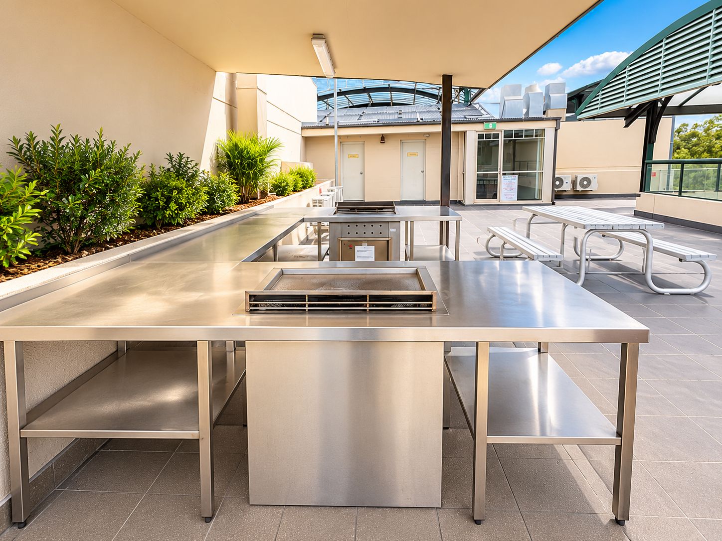 An outdoor patio area with a stainless steel table, benches, and a grill.