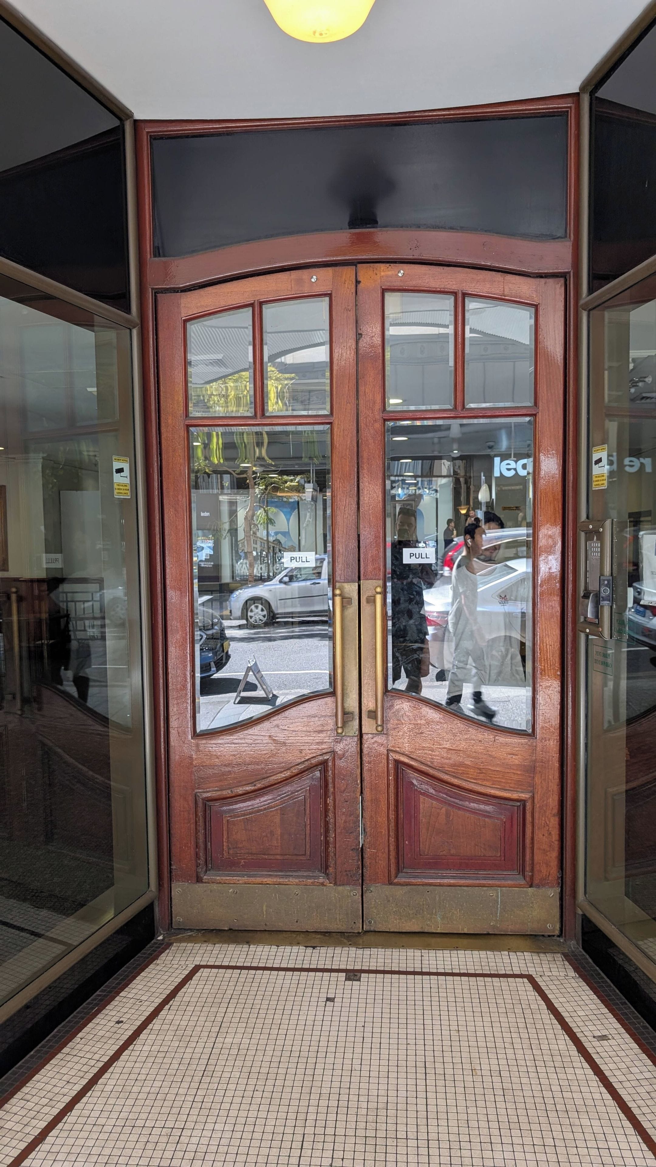 Una puerta de madera giratoria con paneles de vidrio, piso de baldosas y un letrero que indica 'PULL'.