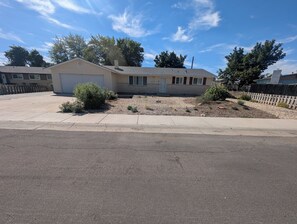 A single-story house with a garage, a small front yard with landscaping, and a clear blue sky.