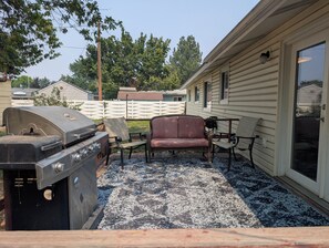 A patio area with a grill, two chairs, and a table.
