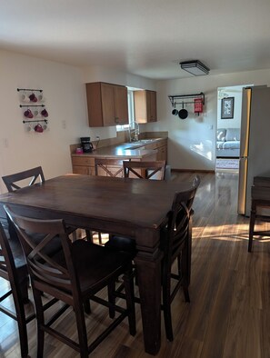 A kitchen with wooden cabinets, a dining table with chairs, and a view into a living area.