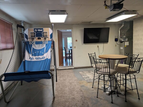 A room with a basketball hoop, a TV mounted on the wall, and a round table with chairs.