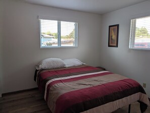 A bedroom with a bed, two windows, and a framed picture on the wall.