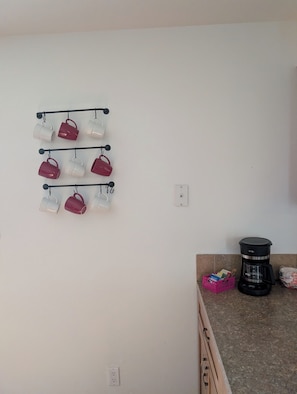 A kitchen with a coffee maker, a pink basket with items, and a wall-mounted mug rack.