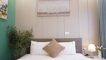 A hotel room with a bed, a wall-mounted artwork, a potted plant, and a nightstand with a lamp.