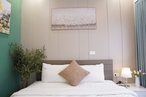 Quarto de hotel com cama, obra de arte na parede, planta em vaso e mesa de cabeceira com abajur.