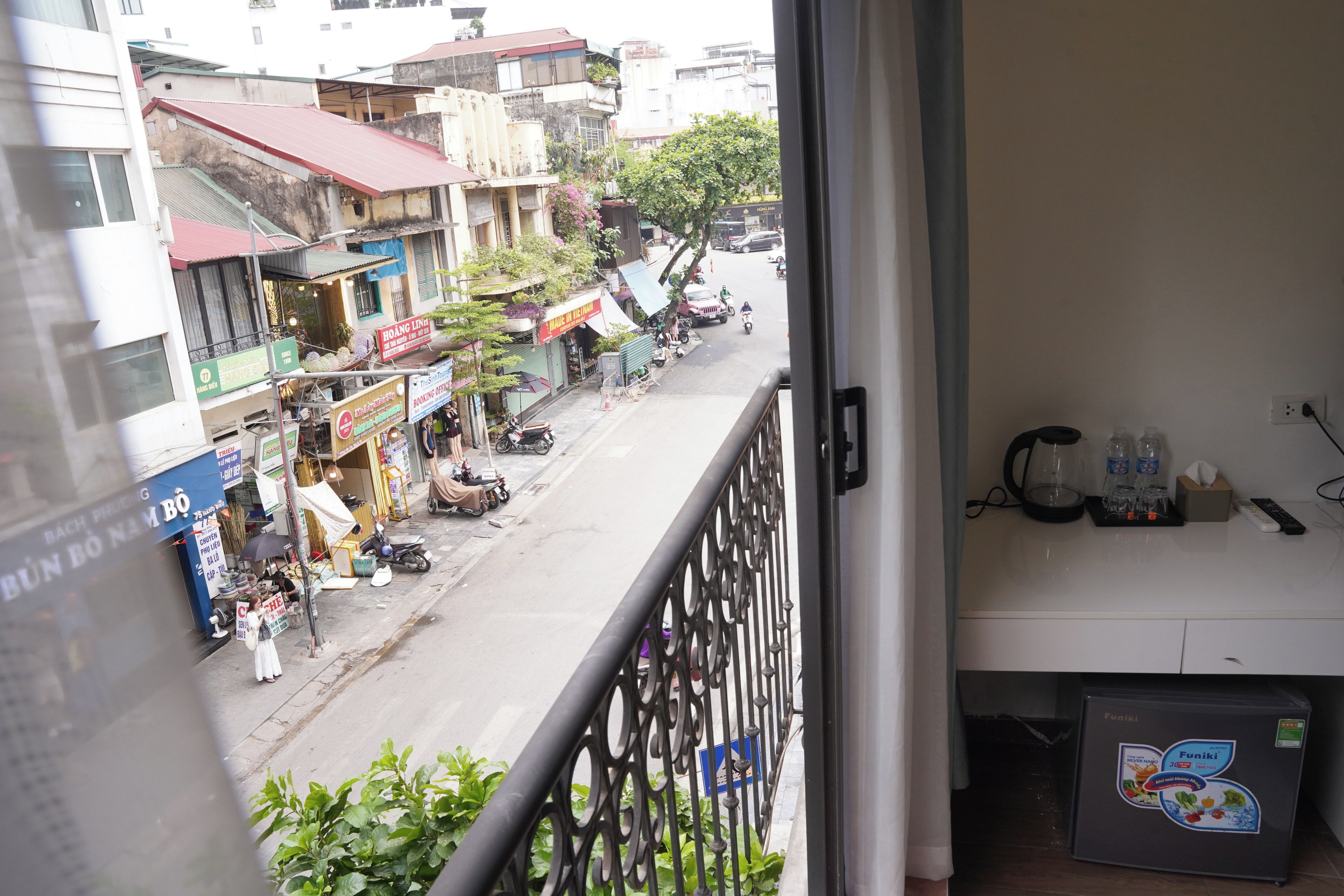 A balcony with a view of a street, a refrigerator, and a power outlet.