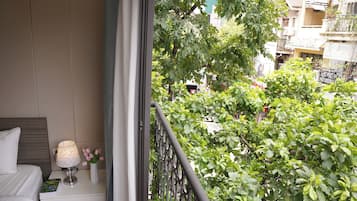 A balcony with a bed, a lamp, and a view of a green area with trees and buildings.