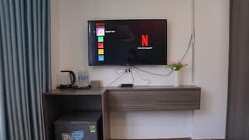 Una sala moderna con un televisor de pantalla plana montado en la pared, una cafetera, una botella de agua, un refrigerador pequeño y un jarrón con flores.