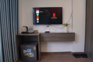 Uma sala de estar moderna com televisão de tela plana na parede, cafeteira, garrafa de água, mini-geladeira e um vaso com flores.