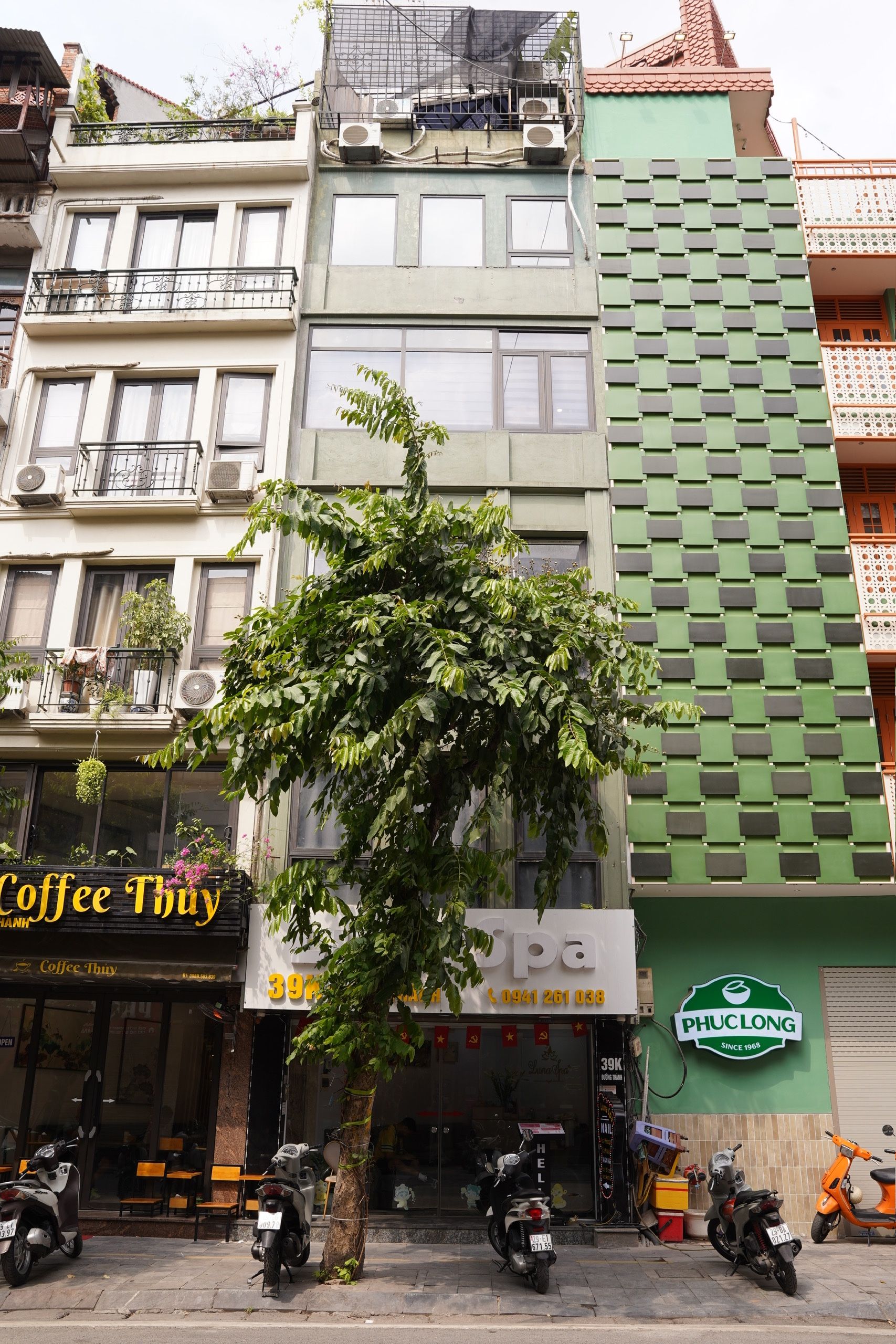 A building with a green facade, a tree in front, and a sign for 'Coffee Thuy' on the ground floor.