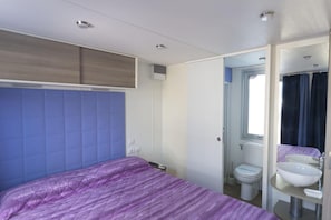 Ein Schlafzimmer mit Bett, Kleiderschrank, Fenster und einem Badezimmer mit Waschbecken und Toilette.