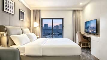 A hotel room with a bed, a desk, a chair, a television, and a city view.