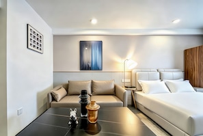 Una habitación de hotel moderna con sofá, cama, una mesita con objetos decorativos y una obra de arte colgada en la pared.