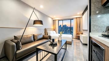 A modern hotel room with a sofa, a bed, a dining table, and a city view.