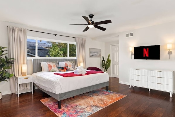 Un dormitorio moderno con cama, mesitas de noche, ventilador de techo, televisor y radiador.