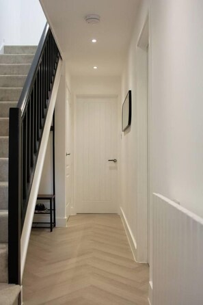 Ein Flur mit Holzboden, einer weißen Tür und einem schwarzen Geländer an einer Treppe.