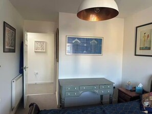 A bedroom with a bed, a dresser, a radiator, a door, and a ceiling light fixture. - Charming Corsham Apartment With 2 Bedrooms (Corsham)
