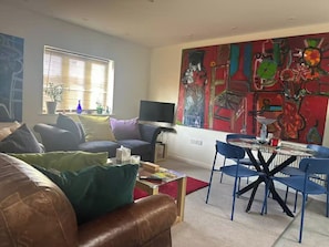 A living room with a brown leather sofa, a glass coffee table, and a dining area with blue chairs and a glass table. - Charming Corsham Apartment With 2 Bedrooms (Corsham)