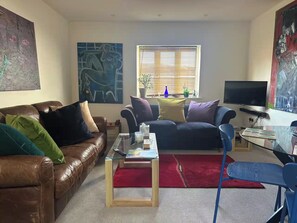A living room with a brown leather sofa, a glass coffee table, a red rug, and a television on a stand. - Charming Corsham Apartment With 2 Bedrooms (Corsham)