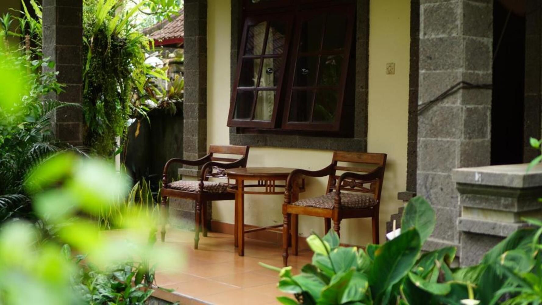An outdoor seating area with two wooden chairs and a table, surrounded by greenery.